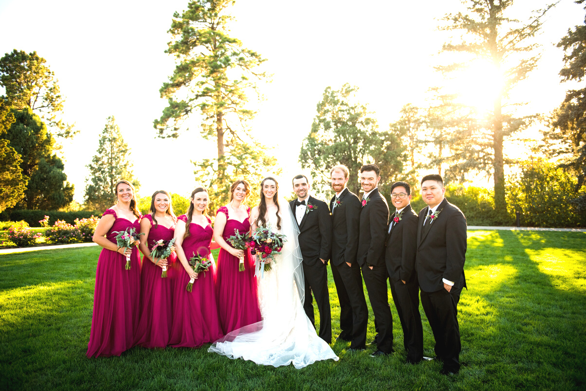 A group of bridesmaids and groomsmen pose for a photo in front of the sun at golden hour at Highlands Ranch Mansion.