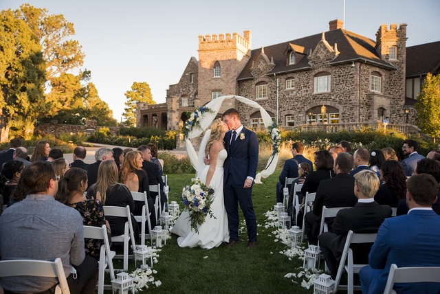 A bride and groom kissing at the end of their wedding ceremony in front of the castle at The Highlands Ranch Mansion.