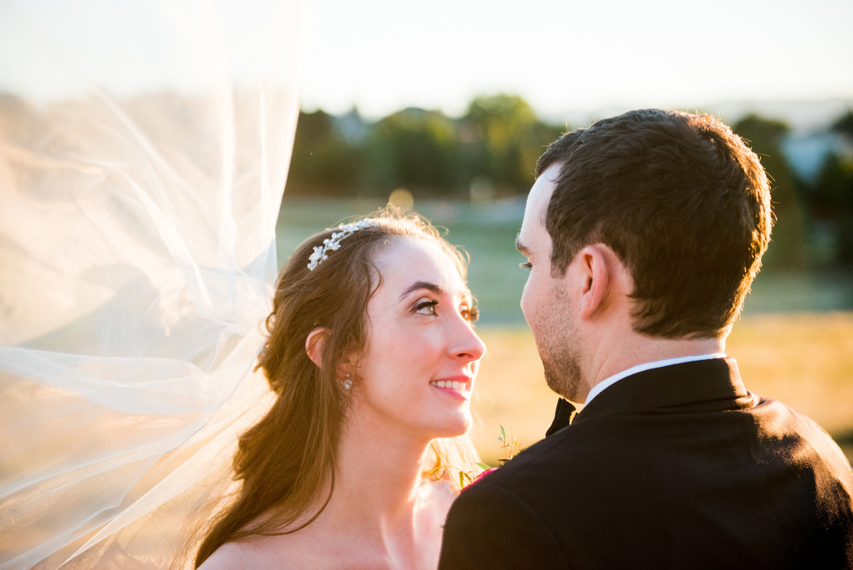 A bride and groom look into each other's eyes under her veil at golden hour.
