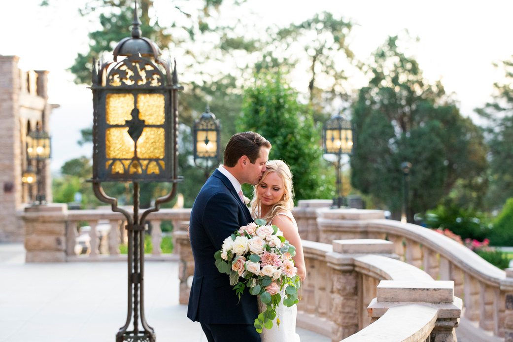 A groom kissing his bride on the temple on the balcony at Highlands Ranch Mansion.