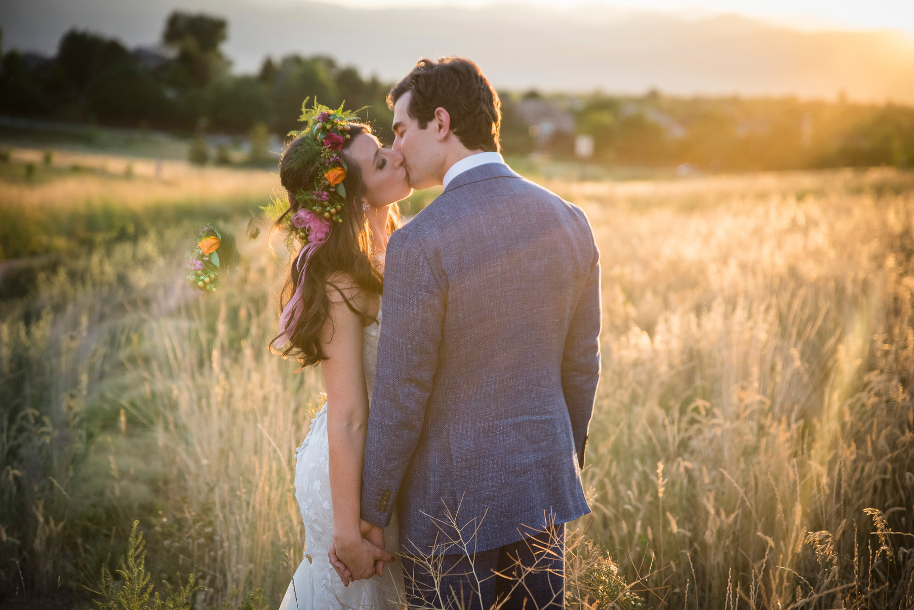 The bride and groom share a kiss in the middle of a field at sunset.