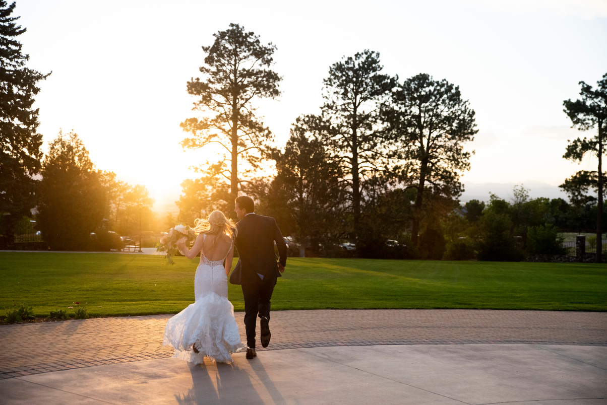 A bride and groom playfully run away from the camera at sunset.