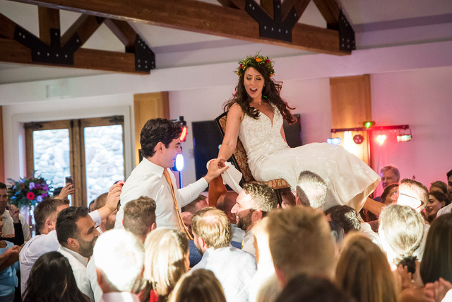 A bride and groom lifted in chairs by their wedding guests during their wedding reception.